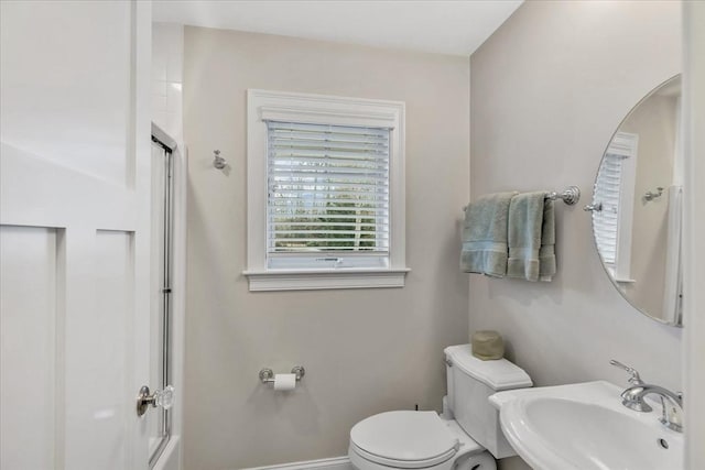 full bathroom featuring sink, bath / shower combo with glass door, and toilet