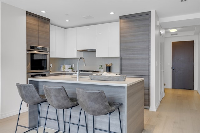 kitchen featuring light wood-type flooring, a breakfast bar area, an island with sink, and stainless steel double oven