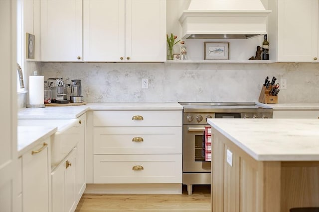 kitchen featuring premium range hood, high end stainless steel range, light wood-type flooring, and backsplash