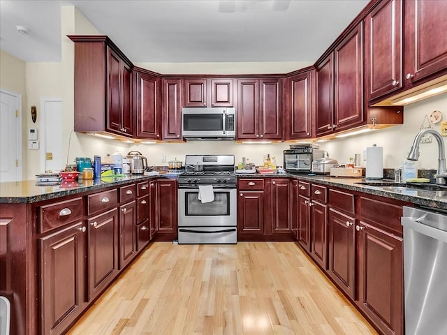 kitchen with stainless steel appliances, sink, dark stone countertops, and light wood-type flooring