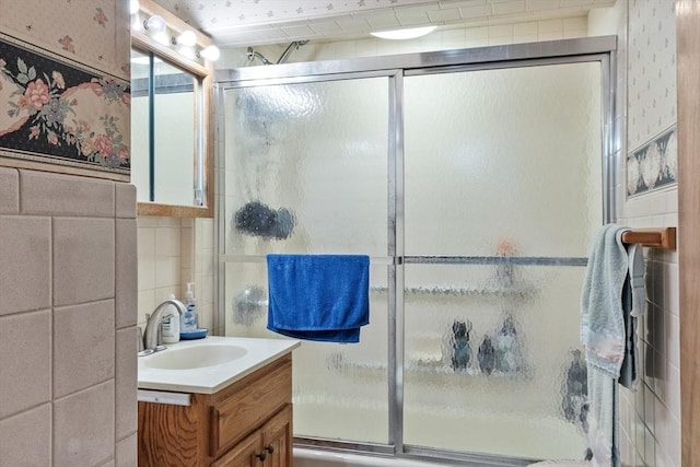 full bath with vanity, shower / bath combination with glass door, tile walls, and wallpapered walls