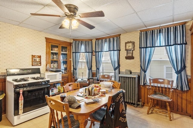 dining space with wallpapered walls, radiator, a drop ceiling, a ceiling fan, and light floors