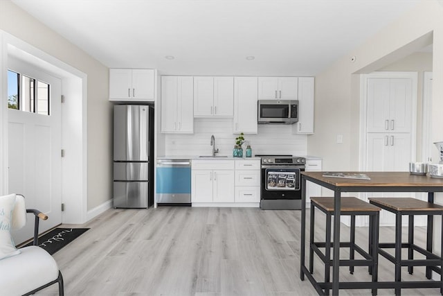 112 W Main Unit 5, Barnstable, MA 02601 - kitchen with stainless steel appliances, decorative backsplash, white cabinetry, light wood-style flooring, and light countertops