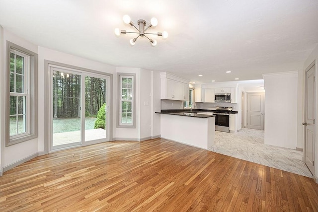kitchen with appliances with stainless steel finishes, light wood-type flooring, a chandelier, a peninsula, and white cabinets