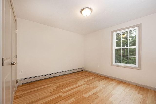 empty room with a baseboard heating unit, light wood finished floors, and baseboards
