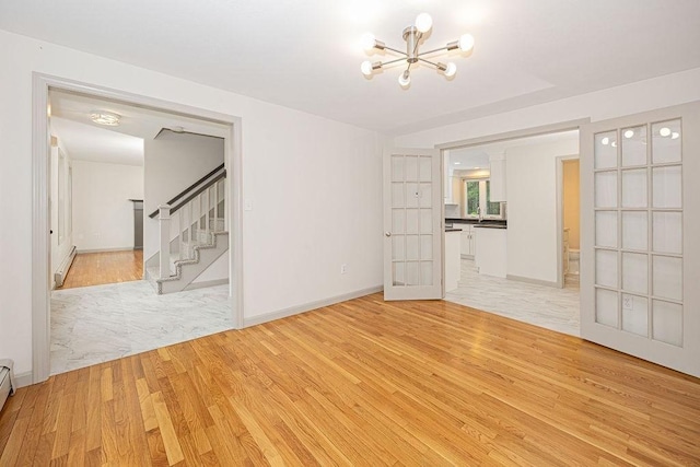 unfurnished room with light wood-style floors, stairs, a baseboard heating unit, and a chandelier