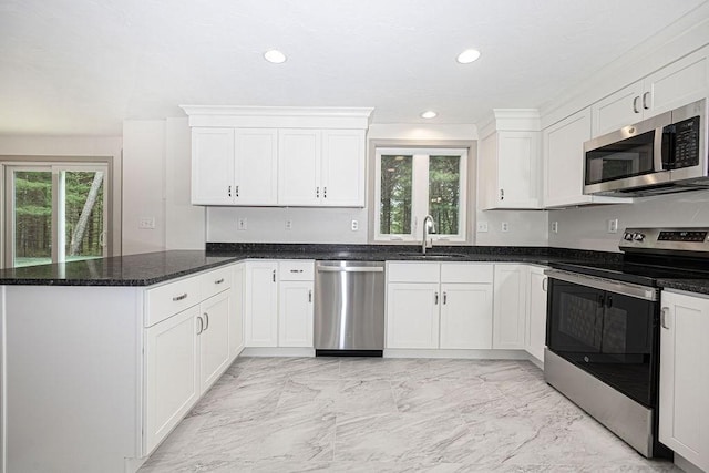 kitchen with appliances with stainless steel finishes, a sink, a peninsula, light marble finish floors, and white cabinets