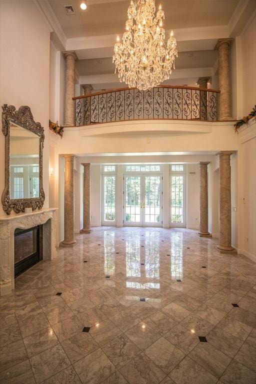 unfurnished living room featuring french doors, ornate columns, an inviting chandelier, a towering ceiling, and a fireplace