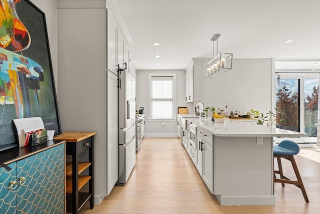 kitchen featuring light countertops, stainless steel gas range, light wood-type flooring, a peninsula, and a kitchen breakfast bar