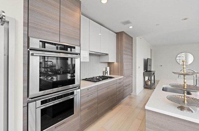 1 Franklin St Unit 1504, Boston, MA 02110 - kitchen with stainless steel gas stovetop, tasteful backsplash, light countertops, light wood-style flooring, and modern cabinets