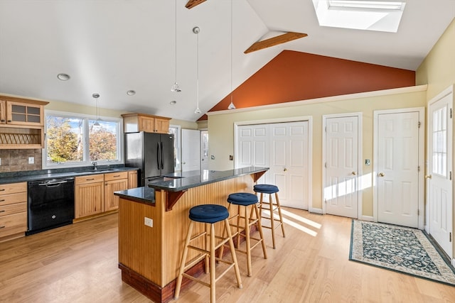 kitchen with a center island, black appliances, a skylight, light wood-type flooring, and decorative light fixtures