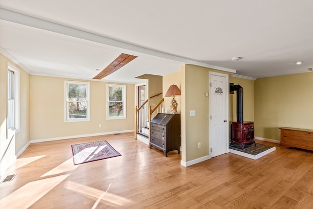 interior space with beam ceiling, a wood stove, light hardwood / wood-style floors, and crown molding