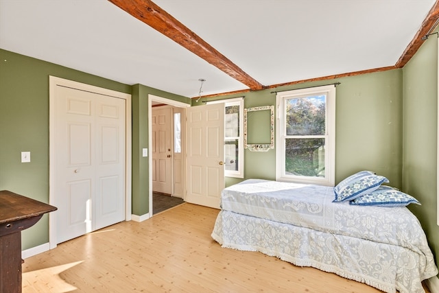 bedroom with light hardwood / wood-style floors, beam ceiling, and a closet