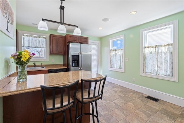 kitchen featuring sink, stainless steel fridge, dishwasher, hanging light fixtures, and a kitchen bar