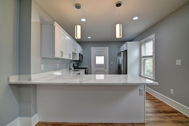 kitchen featuring light stone counters, dark wood finished floors, white cabinetry, appliances with stainless steel finishes, and a peninsula