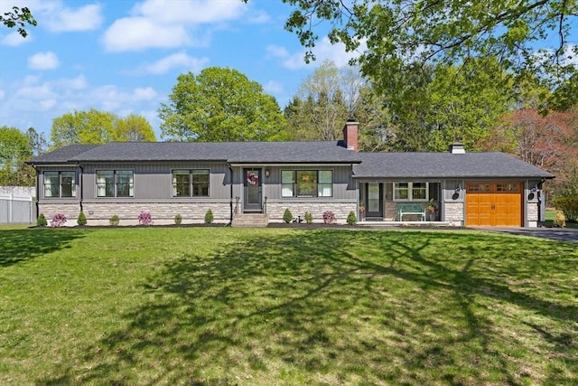 view of front of home with a front lawn, stone siding, a chimney, an attached garage, and driveway