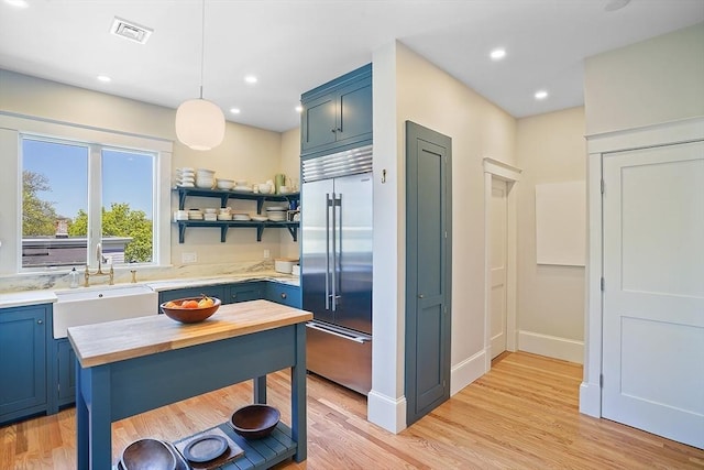 kitchen featuring visible vents, butcher block countertops, stainless steel built in refrigerator, a sink, and blue cabinetry