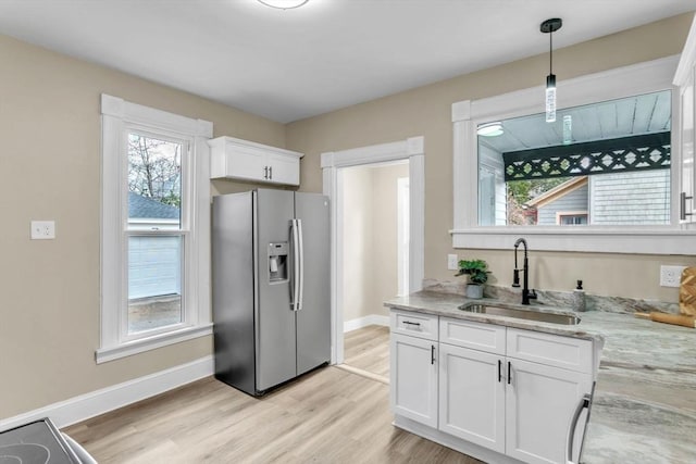 kitchen with stainless steel fridge, light stone counters, sink, decorative light fixtures, and white cabinets