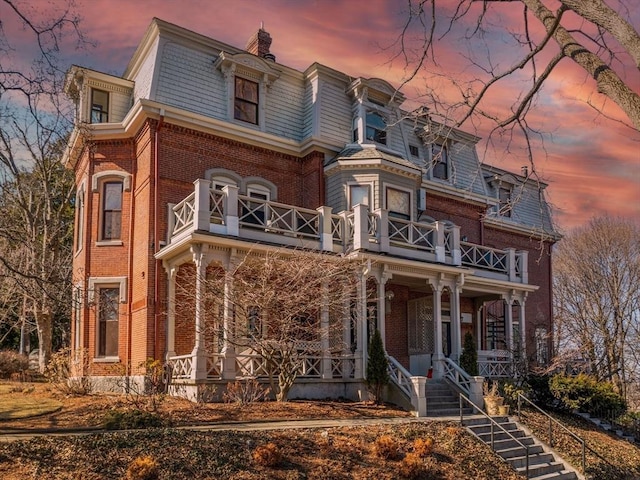 victorian home featuring a high end roof, covered porch, brick siding, and mansard roof