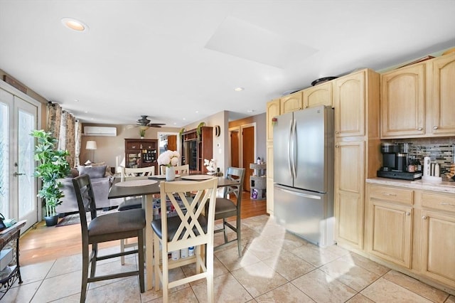 kitchen with light tile patterned floors, stainless steel refrigerator, a wall mounted AC, decorative backsplash, and light brown cabinets