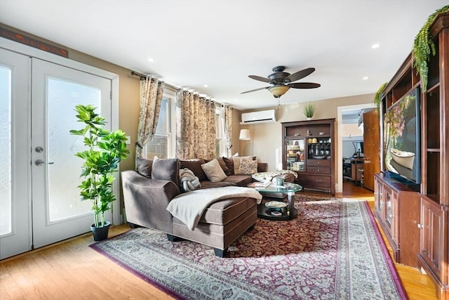 living room with light hardwood / wood-style flooring, a wall mounted air conditioner, ceiling fan, and french doors