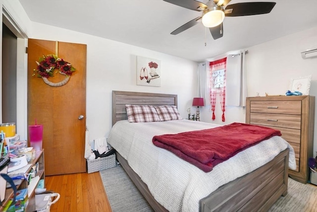 bedroom featuring ceiling fan, a wall mounted AC, and light hardwood / wood-style floors