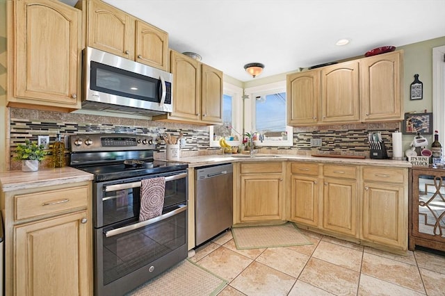 kitchen with light tile patterned flooring, sink, decorative backsplash, stainless steel appliances, and light brown cabinets