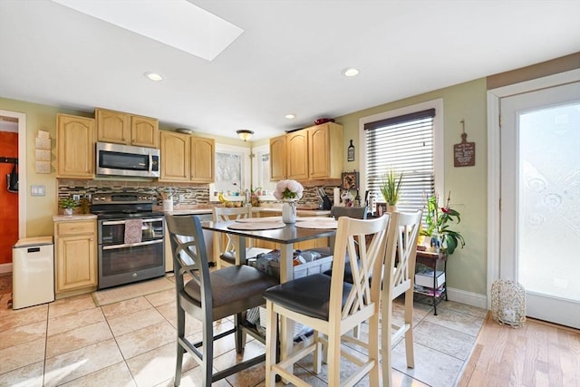 kitchen with light brown cabinetry, a skylight, light tile patterned floors, stainless steel appliances, and backsplash