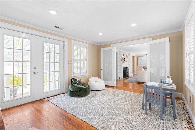 sitting room featuring crown molding, french doors, a fireplace with flush hearth, and wood finished floors