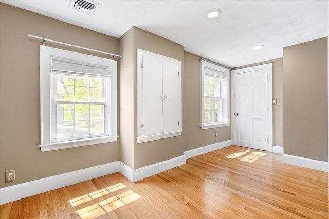 unfurnished bedroom with baseboards, multiple windows, light wood-style flooring, and visible vents