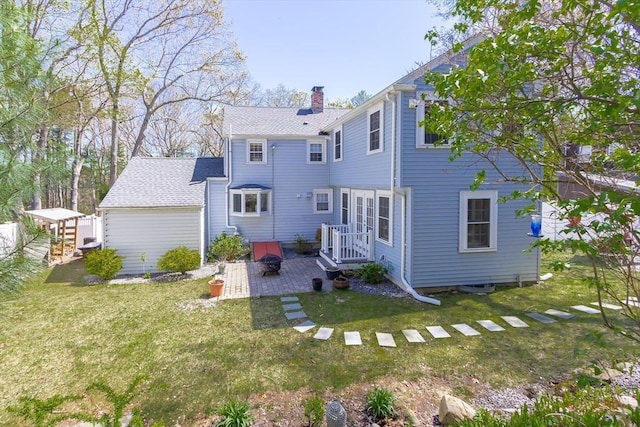 rear view of house with a lawn, a patio, a chimney, and roof with shingles