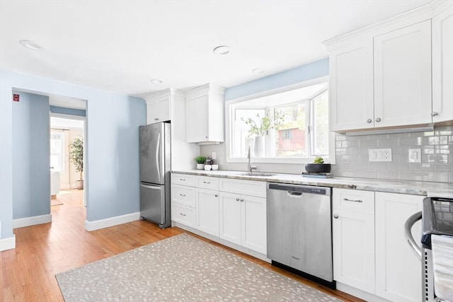 kitchen featuring a sink, light wood finished floors, stainless steel appliances, baseboards, and white cabinetry