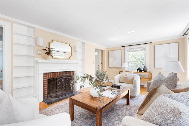 living room featuring ornamental molding, a fireplace, built in shelves, and wood finished floors