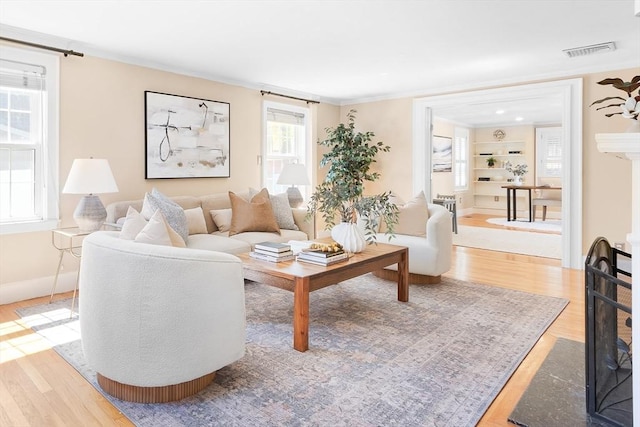 living room featuring baseboards, visible vents, built in shelves, and wood finished floors