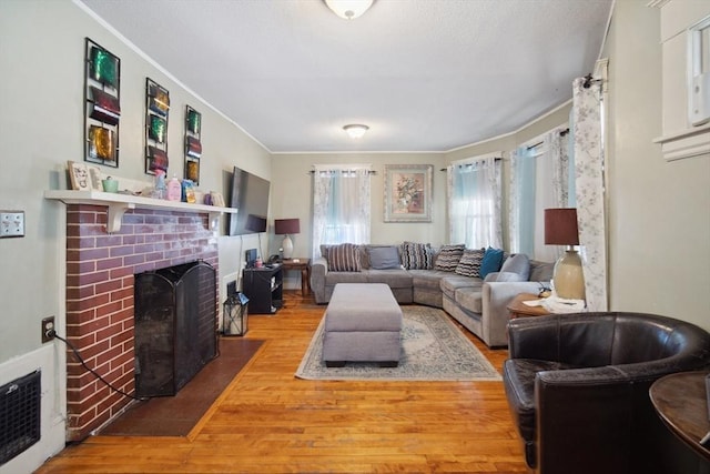 living room featuring heating unit, a brick fireplace, crown molding, and wood-type flooring