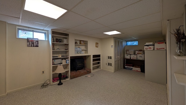 basement featuring a wood stove, a paneled ceiling, and carpet floors