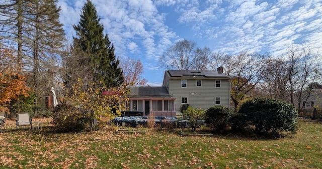 back of property with a sunroom, a yard, and solar panels