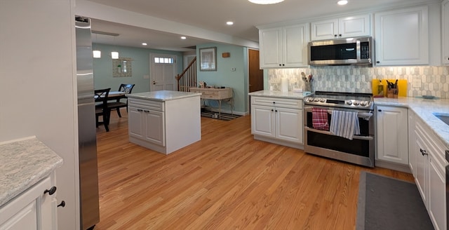 kitchen featuring white cabinets, pendant lighting, stainless steel appliances, and light hardwood / wood-style flooring