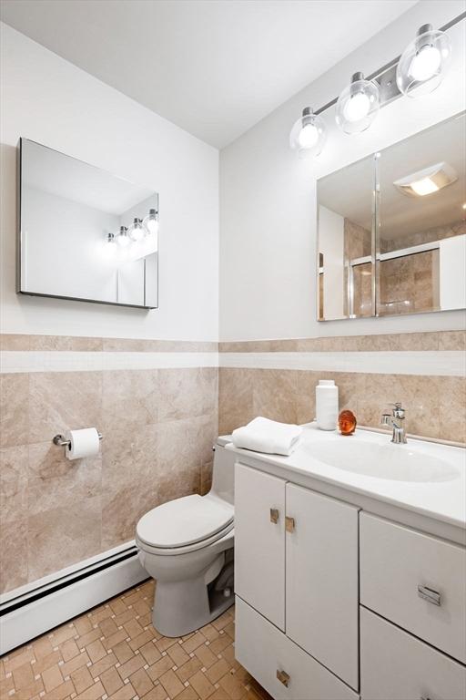 228 Atlantic Ave, Swampscott, MA 01907 - bathroom with tile walls, baseboard heating, toilet, vanity, and wainscoting