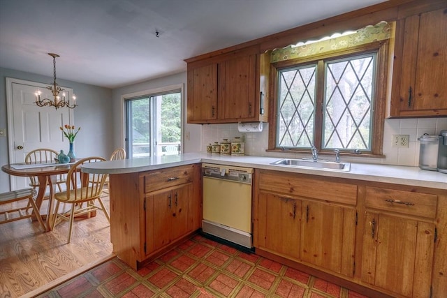 kitchen featuring white dishwasher, a sink, light countertops, and a peninsula