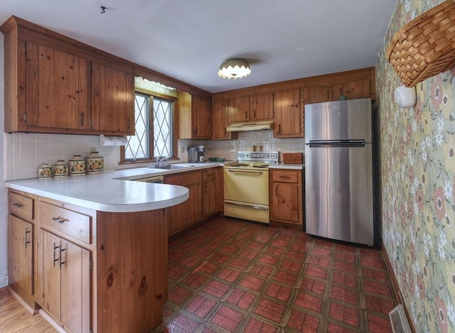 kitchen featuring freestanding refrigerator, white electric range, under cabinet range hood, a peninsula, and a sink