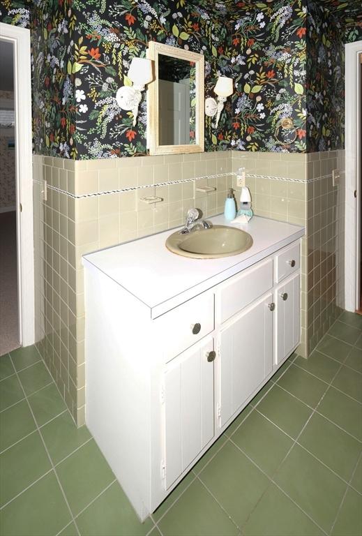 bathroom with wallpapered walls, tile walls, tile patterned floors, wainscoting, and vanity