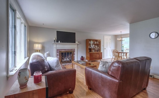 living area featuring a chandelier, wood finished floors, and a brick fireplace