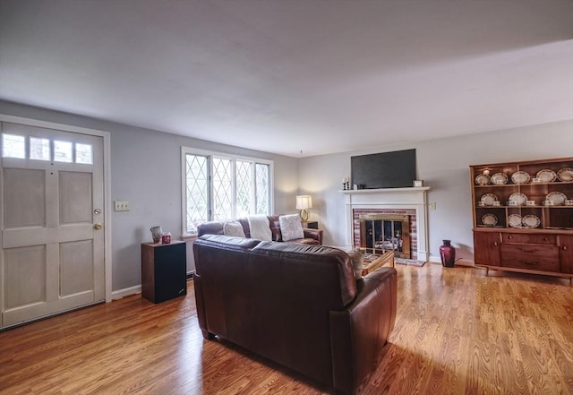 living room featuring wood finished floors, a brick fireplace, and baseboards