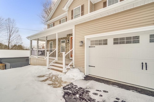 snow covered property entrance featuring a garage and covered porch