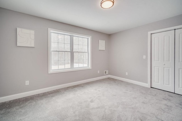 unfurnished bedroom with a closet, light colored carpet, visible vents, and baseboards