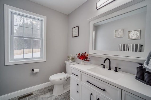 half bath with toilet, vanity, visible vents, and baseboards