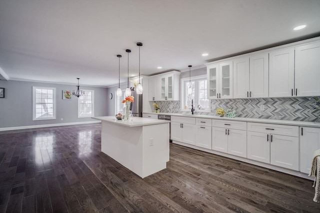 kitchen with glass insert cabinets, a center island, hanging light fixtures, light countertops, and white cabinetry