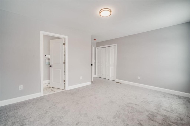 unfurnished bedroom featuring light carpet, a closet, connected bathroom, and baseboards