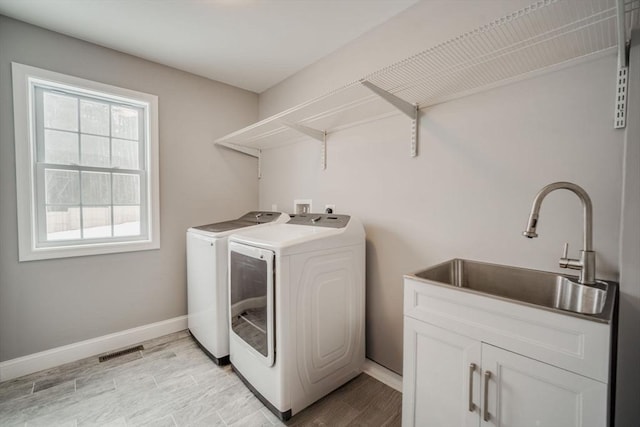 laundry area featuring washing machine and dryer, a sink, visible vents, baseboards, and cabinet space